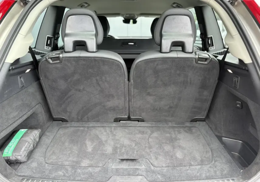 Vue arrière du coffre spacieux d’un Volvo XC90 gris Dusk avec sièges rabattus et kit de premiers secours visible à gauche.