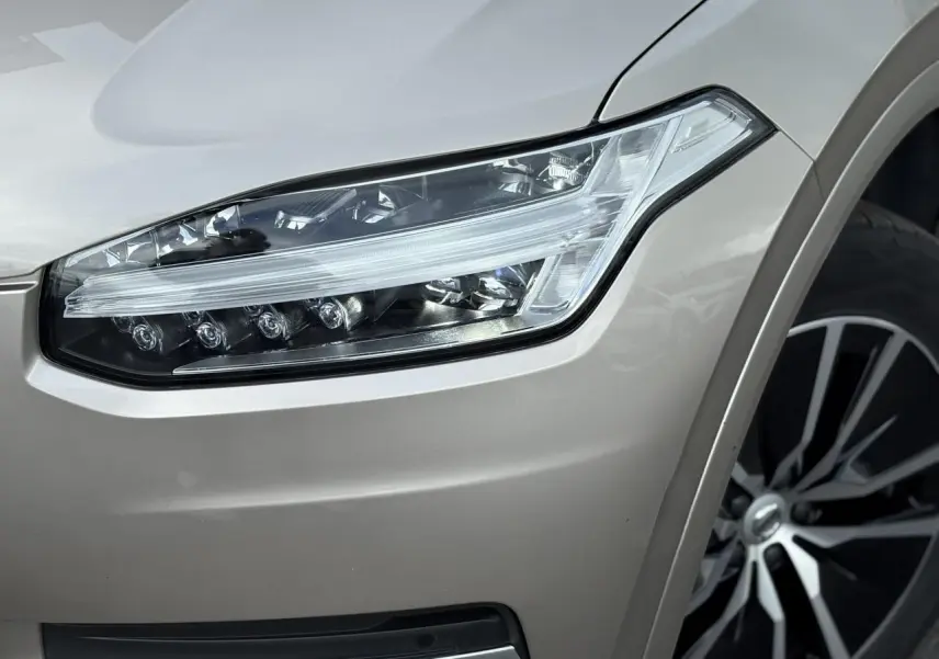 Gros plan sur le phare avant droit et la jante alliage 19 pouces noir diamant du Volvo XC90 gris Dusk.