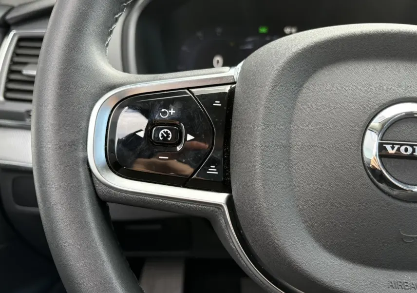 Gros plan sur la partie gauche du volant noir du Volvo XC90 T8 AWD 2024 avec commandes intégrées et logo central.