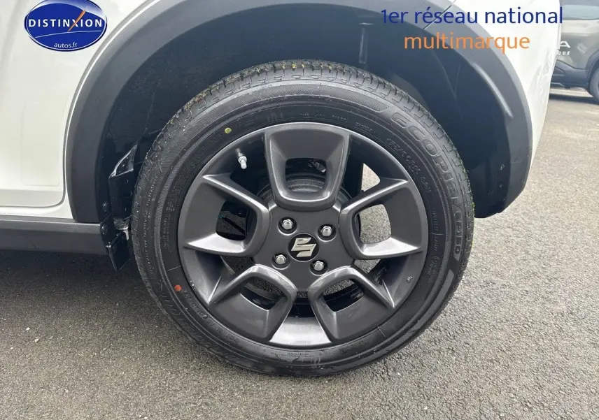 Gros plan sur la roue avant gauche de la Suzuki Ignis 2023 en Pure White Pearl métallisé avec jante alu gris foncé.