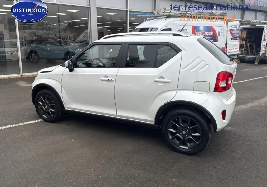 Vue de profil côté gauche d'une Suzuki Ignis blanche nacrée avec jantes noires et barres de toit visibles.