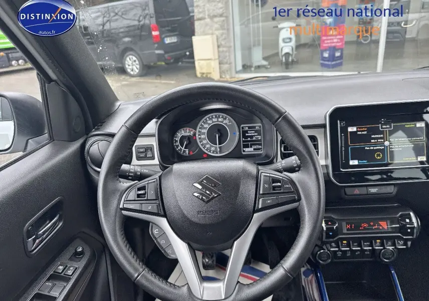 Vue intérieure centrée sur le volant cuir multifonction d'une Suzuki Ignis blanche, avec tableau de bord et écran tactile visibles.