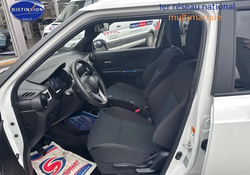 Vue intérieure côté conducteur de la Suzuki Ignis 2023 blanche, montrant sièges et tableau de bord avec volant cuir.
