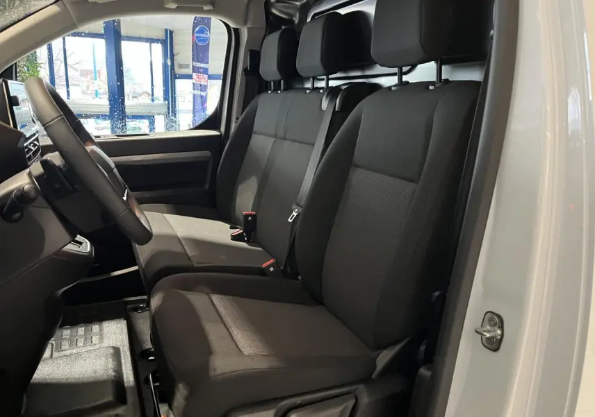 Vue intérieure côté conducteur du Peugeot Expert Fourgon blanc 2024, montrant les sièges tissu bi-ton noir-gris et le volant cuir.