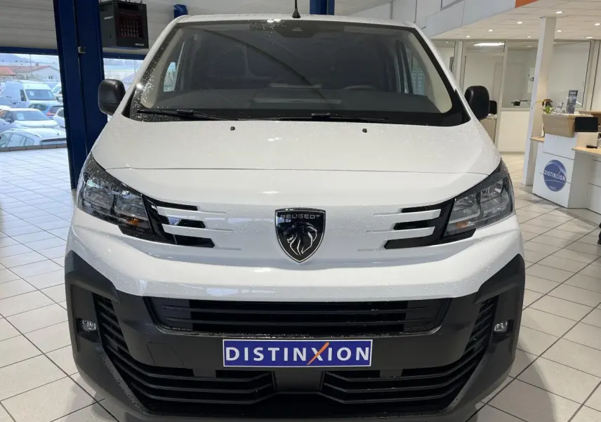 Vue avant du Peugeot Expert Fourgon blanc 2024 avec calandre noire et logo lion central, en intérieur showroom.