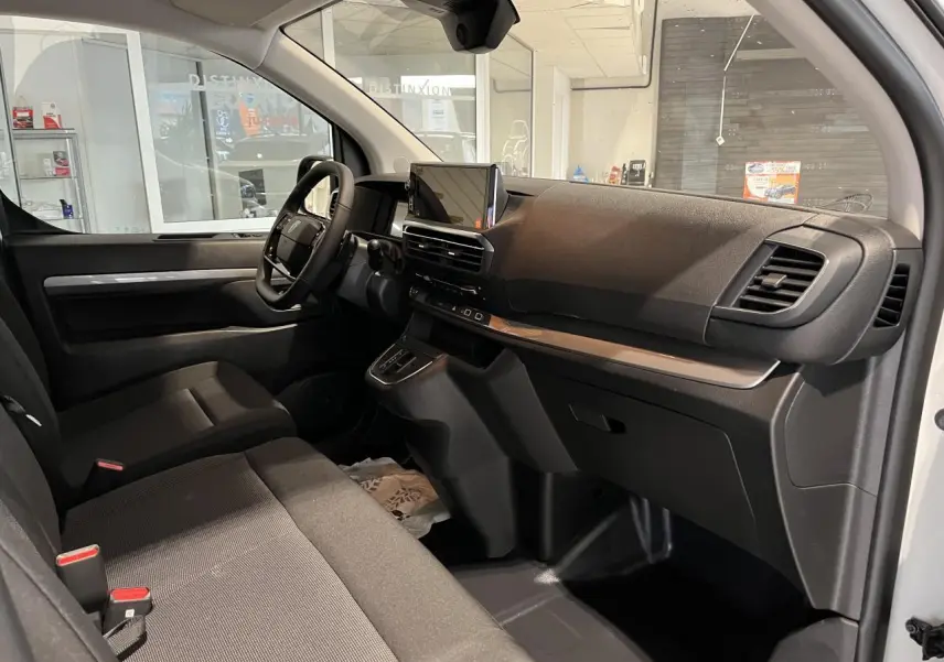 Vue intérieure côté passager du Peugeot Expert Fourgon 2024, montrant la planche de bord noire avec écran tactile et sièges tissu bi-ton noir-gris.