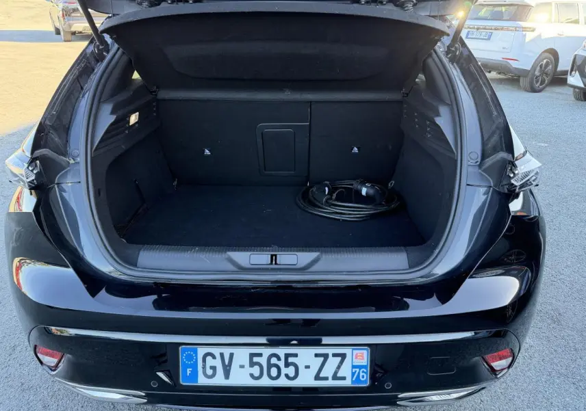Coffre ouvert d'une Peugeot 308 noire vue de l'arrière, avec câble de recharge visible dans le coffre.