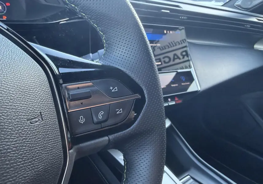 Gros plan sur le volant noir perforé avec surpiqûres vertes et écran tactile du tableau de bord de la Peugeot 308 2024.
