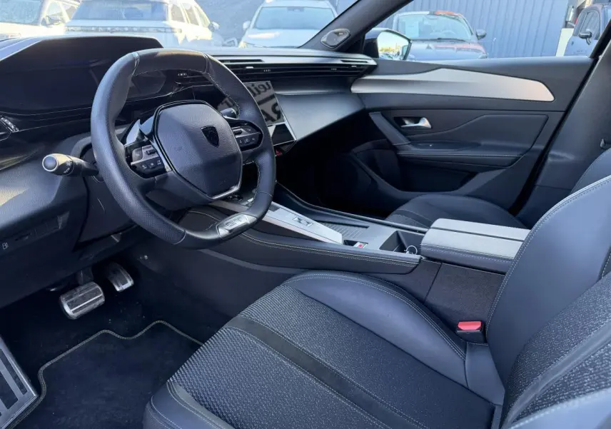 Intérieur avant droit de Peugeot 308 2024 noir, volant compact, sellerie mixte tissu/TEP et console centrale moderne.
