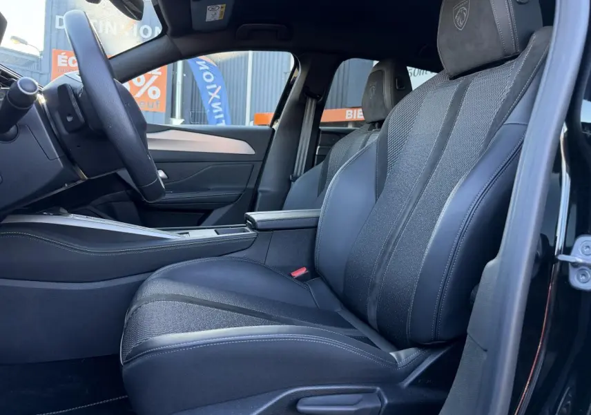 Vue intérieure côté conducteur de la Peugeot 308 2024 noire, sièges tri matières avec logo Lion brodé sur appuie-tête.