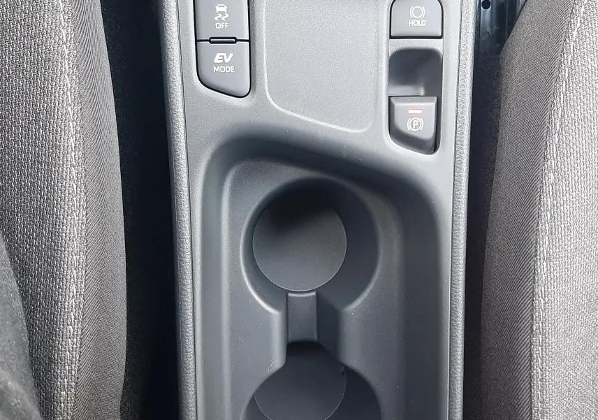 Vue rapprochée de la console centrale grise avec porte-gobelets et boutons de modes de conduite dans une Toyota Yaris Cross 130H Design 2025.