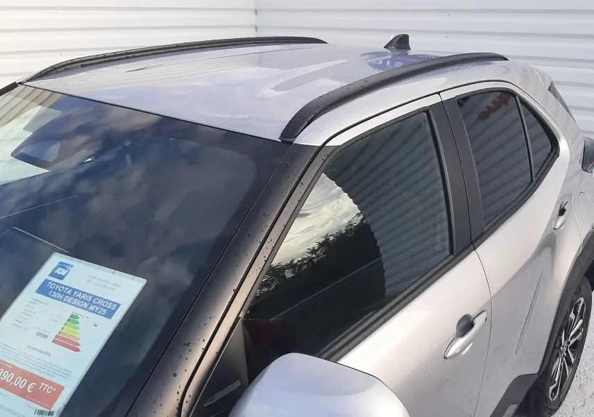 Toyota Yaris Cross 130H Design gris minéral vue 3/4 avant droit avec barres de toit et rétroviseur argenté.