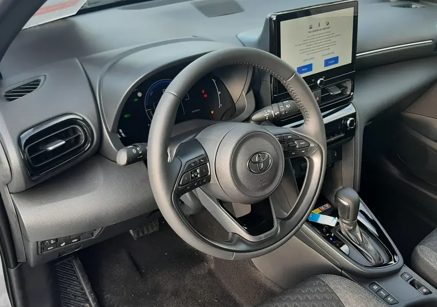 Vue intérieure côté conducteur de la Toyota Yaris Cross 130H Design 2025, tableau de bord noir et écran tactile central.