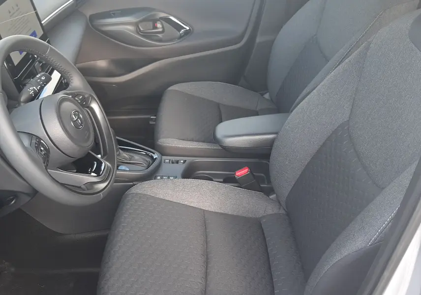 Intérieur avant droit de la Toyota Yaris Cross 130H Design 2025, sièges tissu gris et console centrale avec boîte auto.