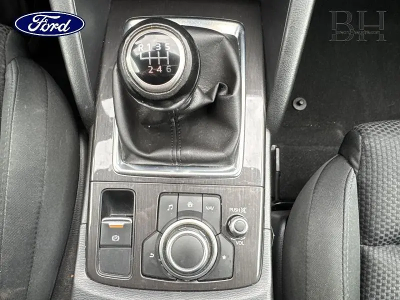 Gros plan sur la commande de boîte manuelle et le système multimédia central d'un Mazda CX-5 blanc, intérieur noir.