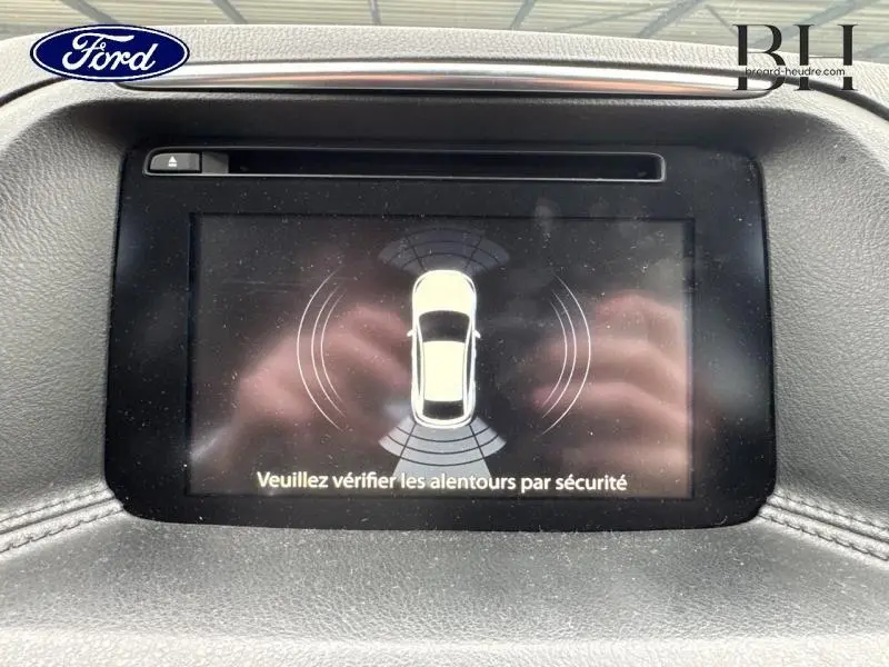 Écran central montrant l’alerte de détection autour d’un Mazda CX-5 blanc, vue intérieure du tableau de bord.