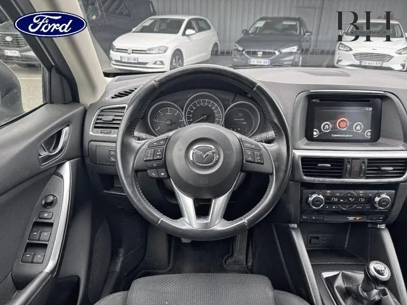 Vue intérieure centrée sur le volant et tableau de bord du Mazda CX-5 blanc, avec commandes au volant et boîte manuelle visible.