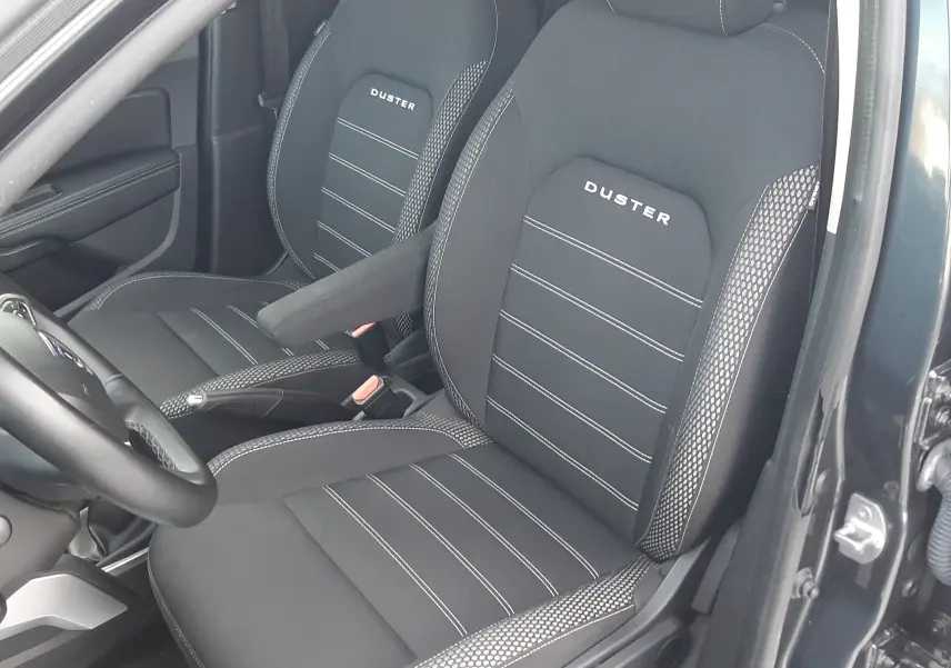 Vue intérieure côté conducteur du Dacia Duster gris Cassiopée 2019, sièges noirs avec logo Duster brodé.