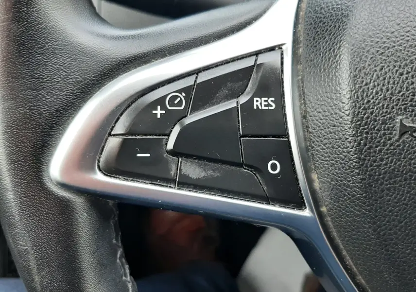 Gros plan sur les commandes de régulateur de vitesse au volant noir du Dacia Duster gris Cassiopée 2019.