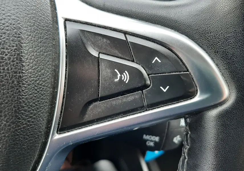 Gros plan sur les commandes vocales et de volume au volant noir du Dacia Duster gris Cassiopée, version 2019.