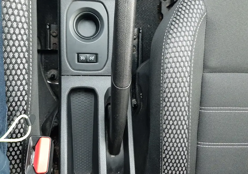 Vue plongeante sur la console centrale du Dacia Duster 2019, frein à main manuel et sièges tissu noir avec surpiqûres grises.
