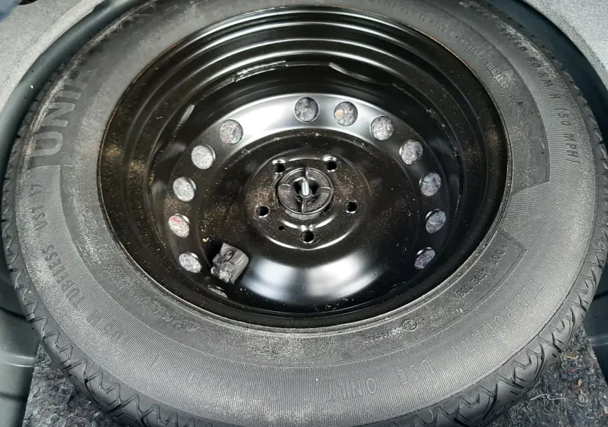 Pneu de secours noir monté sur jante acier visible dans le coffre d'un Dacia Duster gris Cassiopée.