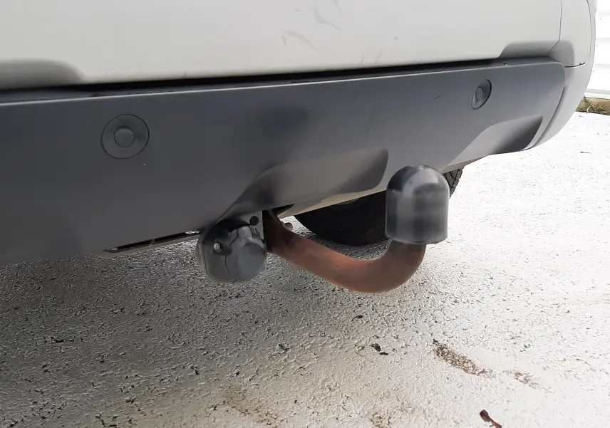 Gros plan sur l'attelage arrière rouillé du Dacia Duster gris cassiopée, avec pare-chocs noir et capuchon de protection.