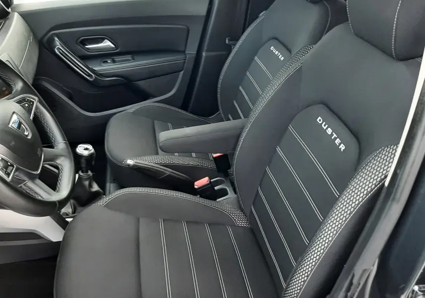 Vue intérieure côté conducteur du Dacia Duster 2019, sièges noirs avec logo DUSTER brodé et coutures contrastées.