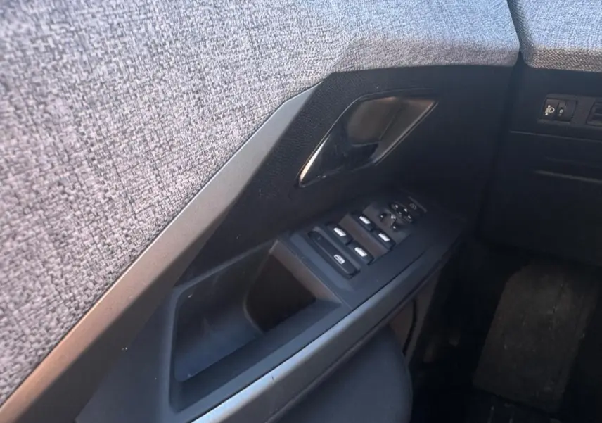 Gros plan sur la commande des vitres et la poignée intérieure côté conducteur du Peugeot 5008 gris Hybrid 145 e-DCS6 Allure 2025.