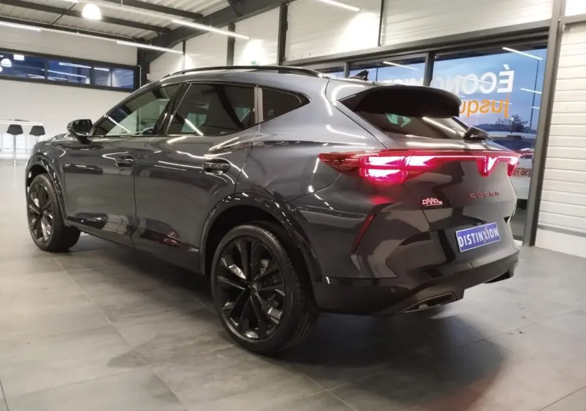 Vue 3/4 arrière droite du CUPRA Formentor gris Magnetic Tech avec jantes noires et feux arrière allumés en intérieur showroom.