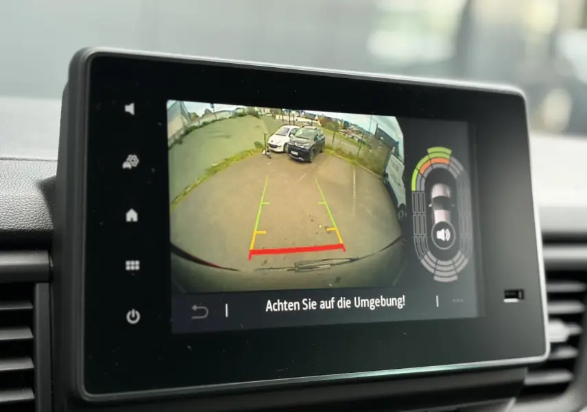 Écran tactile affichant la caméra de recul avec vue arrière sur un parking, dans un Nissan Primastar noir métal.