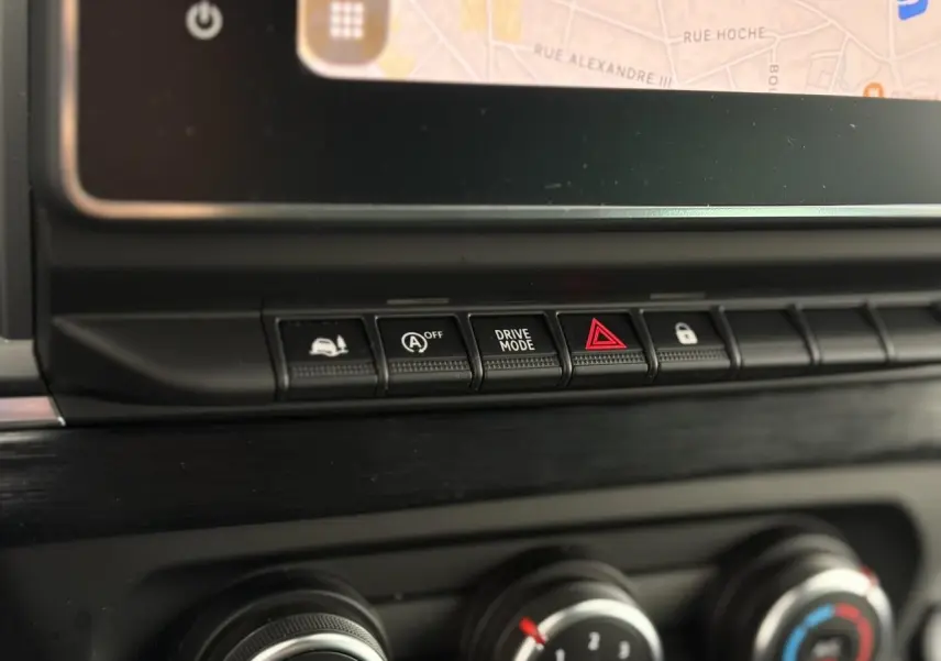 Gros plan sur les commandes centrales noires du tableau de bord du Nissan Primastar 2025, avec écran tactile visible en haut.