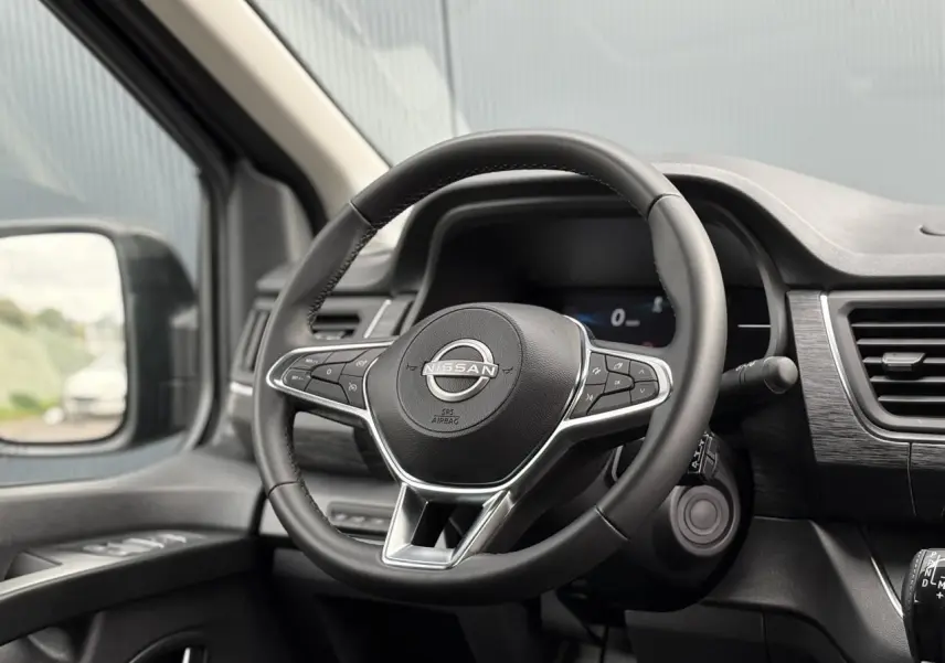 Vue intérieure centrée sur le volant Nissan noir avec commandes intégrées et tableau de bord moderne du Primastar 2025.