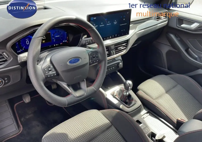 Vue intérieure de la Ford Focus SW 2023, tableau de bord et volant multifonction avec sellerie tissu gris et surpiqûres rouges.