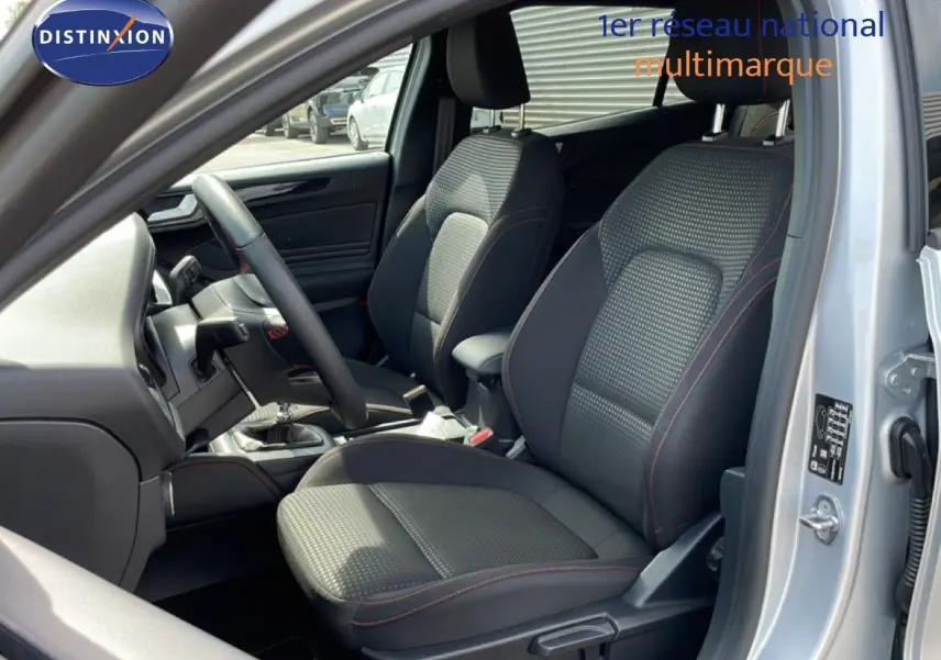 Vue intérieure côté conducteur de la Ford Focus SW gris lunaire, sièges tissu noir avec surpiqûres rouges et volant cuir.