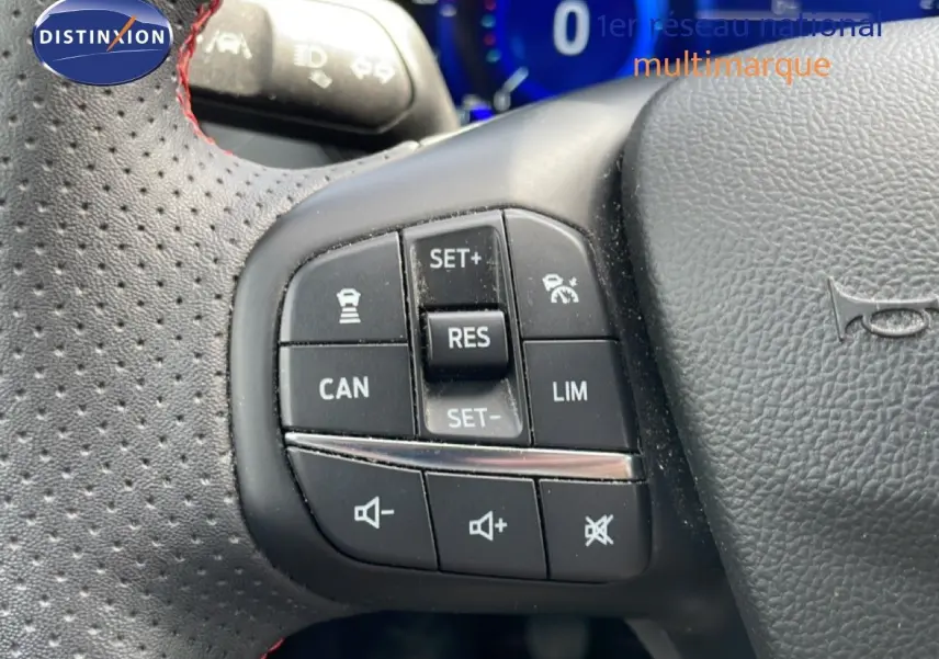 Gros plan sur les commandes noires du volant perforé avec surpiqûres rouges d’une Ford Focus SW gris lunaire 2023.
