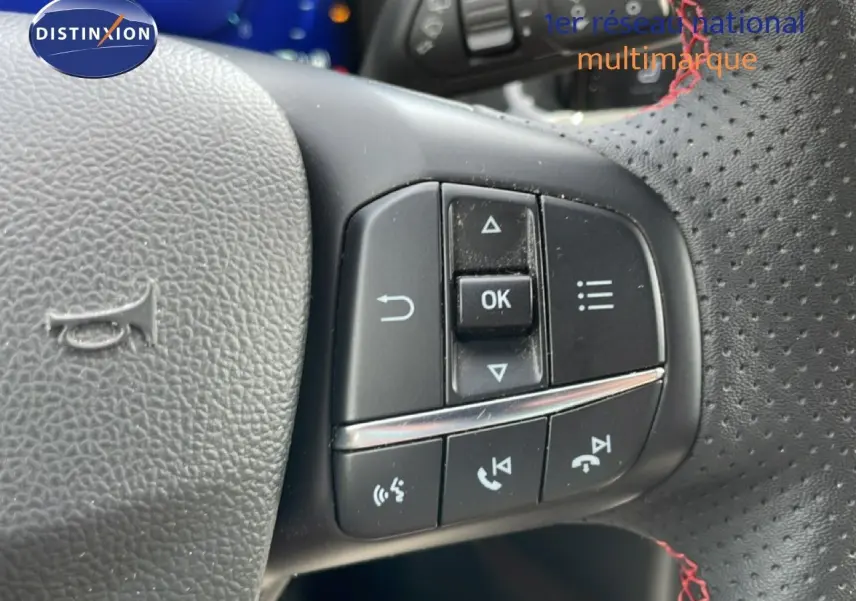 Gros plan sur les commandes multifonctions à droite du volant perforé avec surpiqûres rouges d'une Ford Focus SW gris lunaire 2023.
