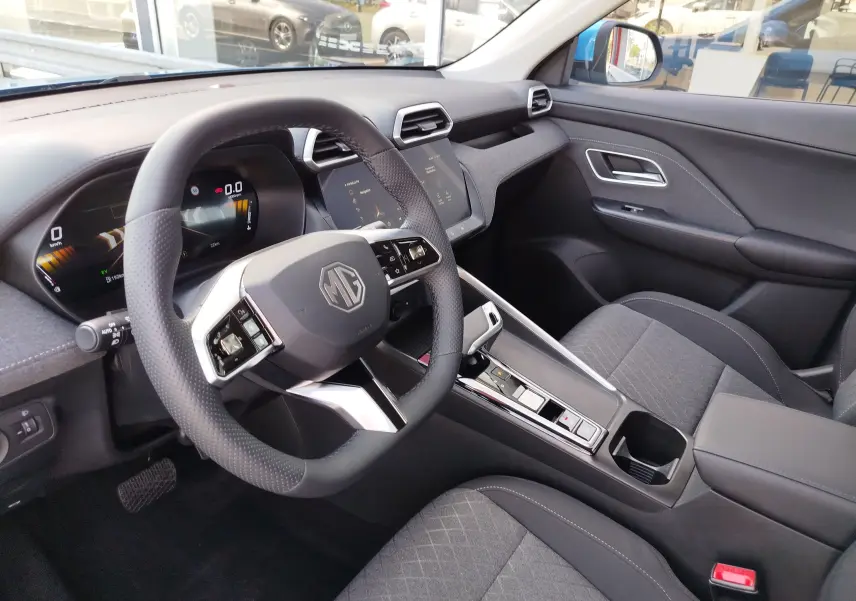 Intérieur de MG ZS 2026 vu côté conducteur, volant multifonction, sièges tissu noir et écran tactile central.
