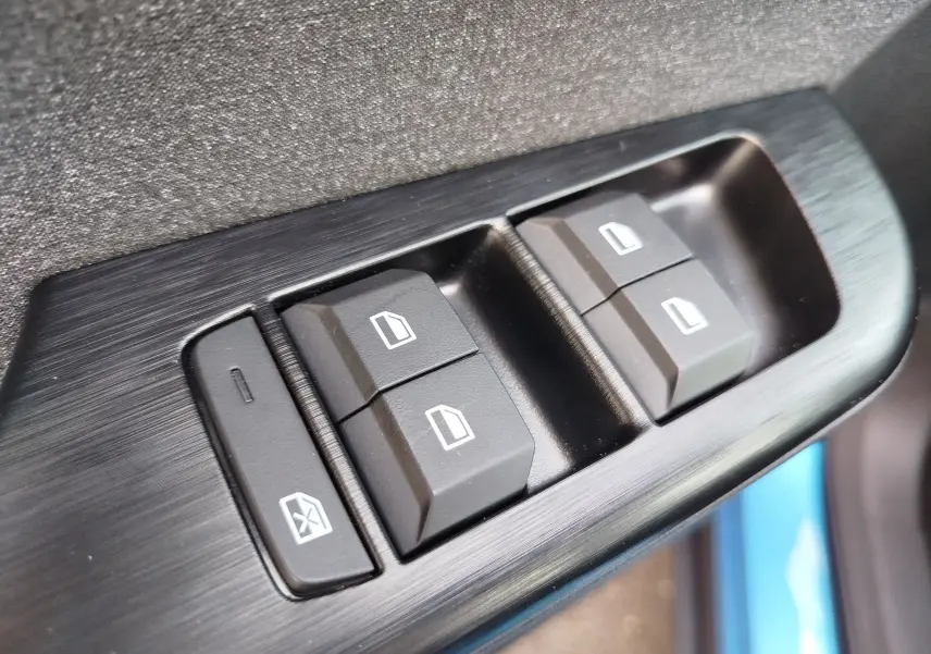 Gros plan sur les commandes des vitres électriques côté conducteur du MG ZS Cosmo Blue, finition noire brossée.