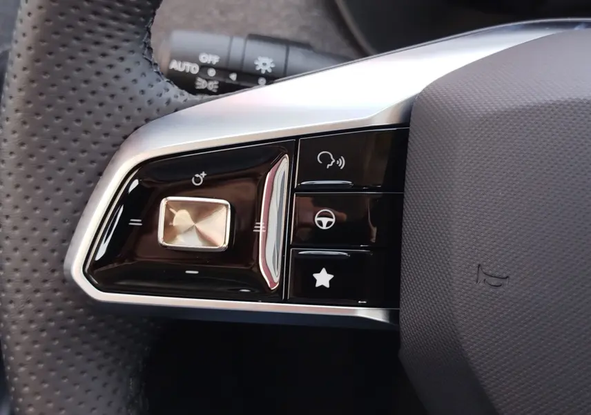 Gros plan sur les commandes gauche du volant noir perforé du MG ZS 1.5 L Hybrid+ 2026 avec finitions argentées.