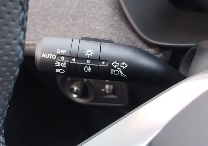 Gros plan sur la commande des feux et clignotants du MG ZS 1.5 L Hybrid+ 2026, intérieur noir et détails gris.