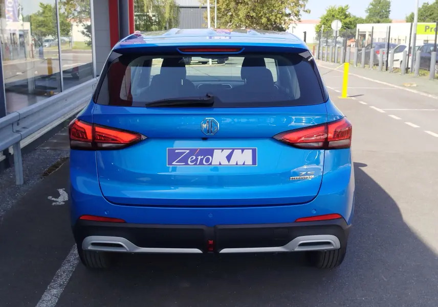 Vue arrière d'un MG ZS hybride bleu Cosmo avec feux arrière LED et logo MG centré sur un parking extérieur.