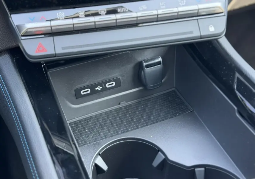 Gros plan sur la console centrale noire du Renault Austral E-Tech avec ports USB-C et rangement devant la commande de climatisation.
