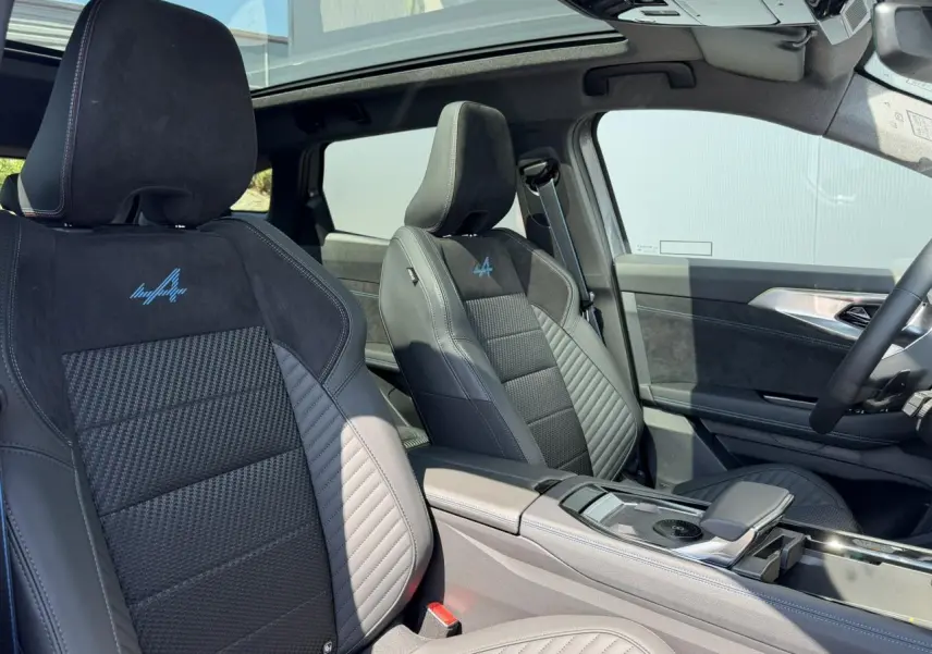 Vue intérieure avant des sièges sport noirs avec logo Alpine bleu, toit panoramique et console centrale du Renault Austral E-Tech.