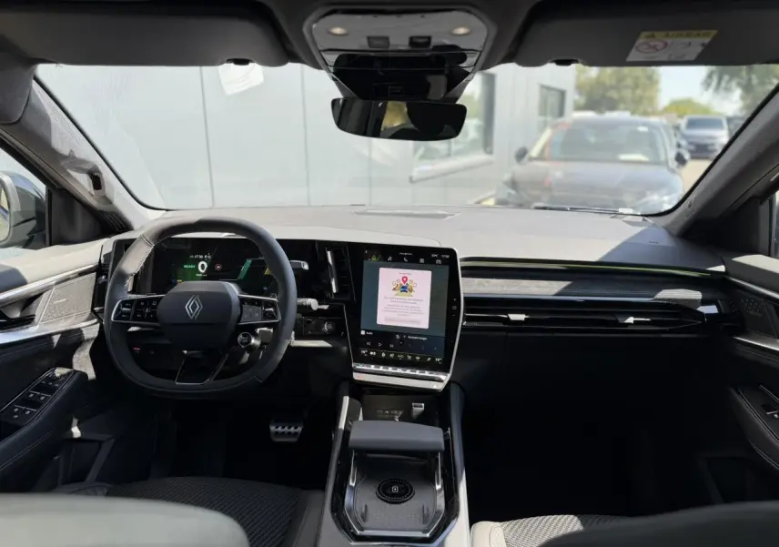 Vue intérieure avant du Renault Austral E-Tech hybride, tableau de bord noir avec écran tactile vertical et volant multifonction.