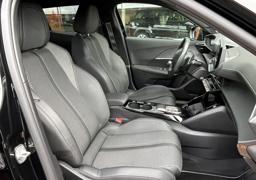 Vue intérieure côté conducteur du Peugeot 2008 noir 2024, mettant en valeur les sièges en cuir et tissu avec surpiqûres contrastées.