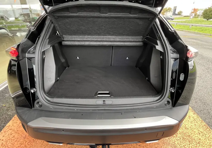 Coffre ouvert vu de l'arrière d'un Peugeot 2008 noir 2024, montrant l'espace de chargement vide et la sellerie sombre.