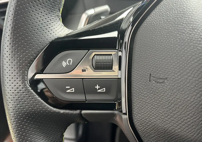 Gros plan sur les commandes gauche du volant noir perforé du Peugeot 2008 2024, avec boutons de volume et commande vocale.