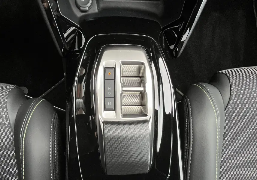 Vue plongeante sur la console centrale noire brillante du Peugeot 2008 2024 avec sélecteur de boîte auto et sièges tissu noir à surpiqûres vertes.