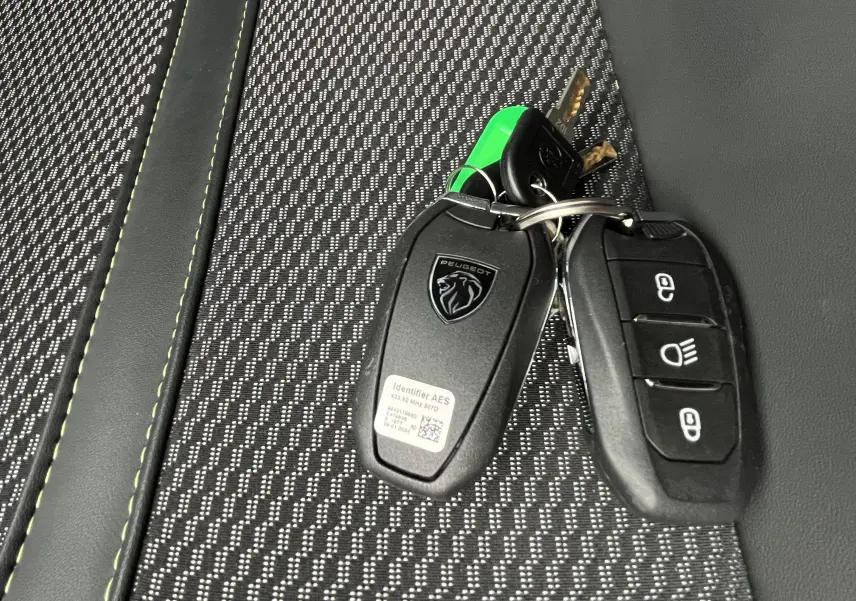 Gros plan sur les clés noires du Peugeot 2008 posées sur un siège en tissu gris à surpiqûres vertes.